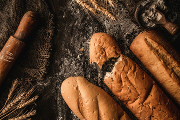 Wall Mural - Freshly bread baguettes on black slate background with wheat spikelets, sackcloth, rolling pin. Pastries and bread in a bakery, Food concept, top view