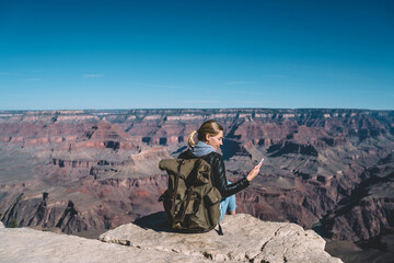 Wall Mural - female traveler holding smartphone checking mobile data connection sitting on mountain top in grand 