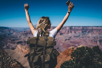 Wall Mural - back view of excited hipster girl standing on high mountain top feeling free raising hands up, happy