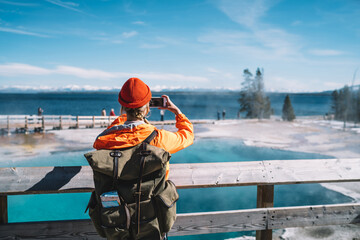 Wall Mural - back view of female tourist with backpack using smartphone for taking picture of hot springs, hipste