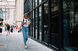 © BullRun - Young female tourist walking on city street with coffee takeaway checking route on mobile application, casually dressed hipster girl reading income message on smartphone strolling in downtown.
