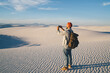 © BullRun - Back view of hipster guy with rucksack making picture on cellphone of scenic horizon over dunes during trip,male traveler shooting video on smartphone enjoying breathtaking panorama of desert