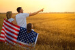 © ZaStock - Back view of a unrecognizable Happy family in wheat field with USA, american flag on back.