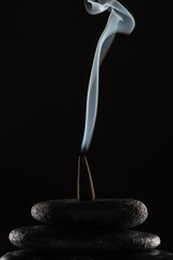 Wall Mural - burning incense cone with smoke on stones on black background