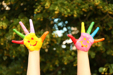 Kid with smiling face drawn on palms in green park, closeup. School holidays