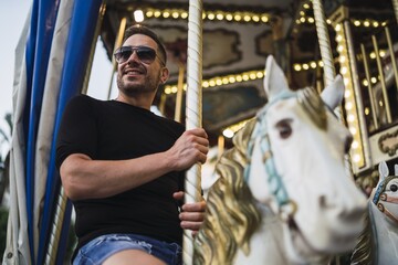 Canvas Print - Young cheerful Caucasian male spending fun time in an attraction park with carousels at daytime