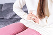 © saran - Young woman suffering from strong abdominal pain or menstruation while sitting on sofa at home. Healthcare medical or daily life concept.