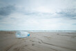 Used plastic bottle on beach with soft wave and cloud in the sky.