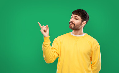 Wall Mural - gesture and people concept - young man in yellow sweatshirt pointing finger to something over emerald green background