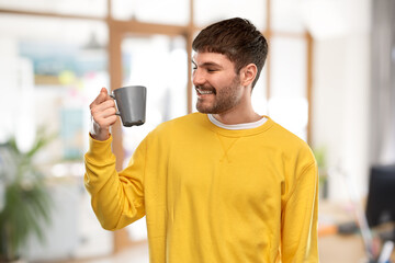 Wall Mural - drinks and people concept - happy smiling young man with coffee cup over office background