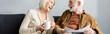 © LIGHTFIELD STUDIOS - horizontal image of senior woman with cup of tea and his husband with newspaper laughing while talking on sofa