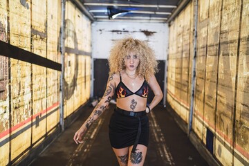 Poster - Attractive young Caucasian female with blonde curly hair and tattoos posing in a garage at daytime