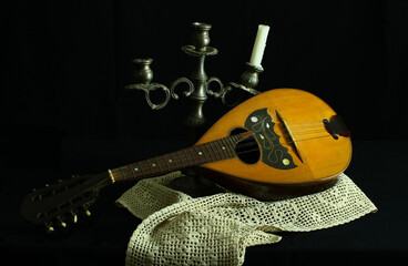 Still life. Antique mandolin and pewter candlestick. Crochet table doily, black background.