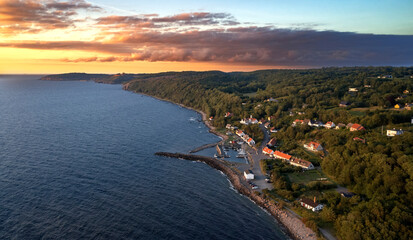 Blick auf den Hafen der dänischen Ortschaft Vang auf der Insel Bornholm in Richtung der alten Festung Hammershus bei einem goldenen Sonnenuntergang vor Wolken im Sommer.