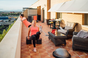 Mother and daughter perform gymnastic exercises on home terrace