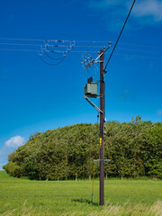 An electricity supply pylon delivering power through the UK national grid showing power cables, isolators and other equipment. Taken on a sunny day with a blue sky.