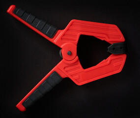 Red spring clamp on dark background. Plastic clamp. Clamping tools for carpentry work