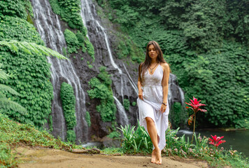 Girl walks in a white dress on a background of a waterfall.