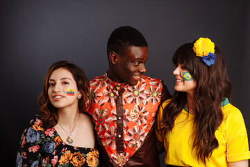 Peaceful Concept of friendship and peace between countries: African man and two Latin ladies in national clothes show hug together with body arts flags Congo, Brazil, Ecuador