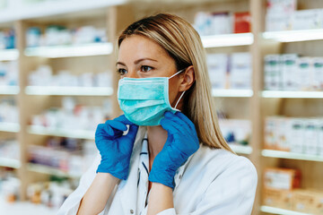 Wall Mural - Female pharmacist with protective mask on her face working at pharmacy. Medical healthcare concept.