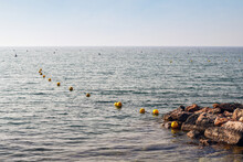 View Of A Lake Shore With A Row Of Yellow Buoys Floating On Water, Lake Garda, Italy