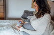© Inti St. Clair - Woman in bed looking at temperature on contactless digital thermometer
