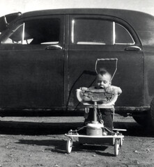 Vintage scene of a toddler eating watermelon beside an antique car