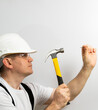 © Dmitry - builder in a white helmet and a white T-shirt with a hammer in his hands hammer a nail.