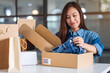 © Farknot Architect - A beautiful young asian woman receiving and opening a postal parcel box of clothing at home for delivery and online shopping concept