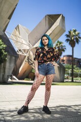 Poster - Vertical shot of an attractive female with blue hair posing in front of a modern building