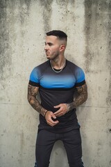 Poster - Vertical shot of Caucasian male with tattoos standing on the wall