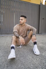 Wall Mural - Vertical shot of a Caucasian male with tattoos wearing fashionable clothes posing on the road