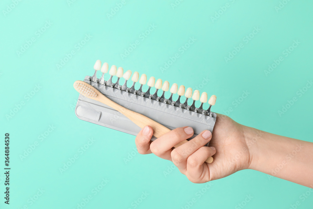 Female hand with toothbrush and teeth samples on color background