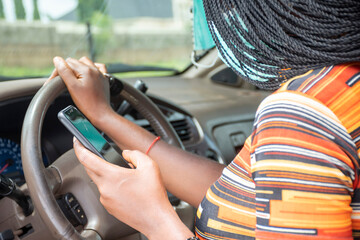 young black woman using her phone while sitting in a car, wearing a face mask