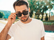 © halayalex - Portrait of handsome smiling stylish hipster lambersexual model.Man dressed in white T-shirt. Fashion male posing on the street background in sunglasses outdoors