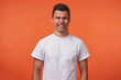 © timtimphoto - Portrait of young brunette male with short haircut grimacing his face and showing teeth while looking at camera, standing over orange background with hands down