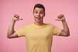 © timtimphoto - Agitated young lovely brown-eyed brunette male looking cheerfully at camera while showing on himself with raised hands, isolated over pink background