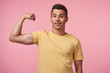 © timtimphoto - Self-confident young pretty short haired brunette guy keeping hand raised while showing his power and looking glaldy at camera, isolated over pink background