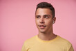 © timtimphoto - Portrait of positive young handsome short haired brunette male with earpiece looking wonderingly aside while standing over pink background with hands down