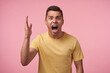 © timtimphoto - Irritated young short haired brunette man with short haircut screaming crossly with wide mouth opened and raising emotionally palm while posing over pink background