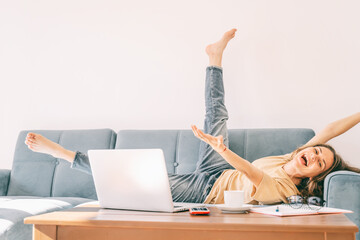 Young beautiful curly woman happy lies on the sofa, on the table a laptop and working papers, success in work