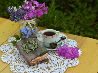 Still life with decorated diary, bunch of wildflowers and cup of tea in the garden. Esoteric, gothic and occult background with magic objects, mystic and fairy tale concept