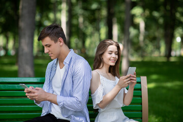 Wall Mural - Gadget addiction. Millennial couple busy with smartphones, talking to virtual friends and ignoring each other at park