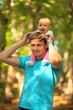 © Sk Elena - The child sits on his fathers shoulders. Father and baby walking in the park. Summer time. Happy family spent time together outdoors.