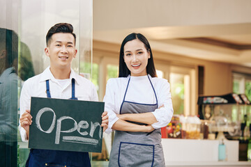 Sticker - Smiling young Vietnamese cafe owners with open sign standing at cafe entrance and welcoming customers inside