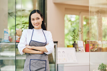 Wall Mural - Portrait of pretty young smiling small coffeeshop owner standing at entrance