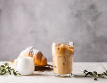 Cold Black Coffee With Ice Cubes In Tall Glass And Fresh Croissant. Refreshing Coffee Drink On A Table Gray Background.