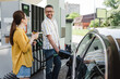 © LIGHTFIELD STUDIOS - Selective focus of smiling man looking at wife with coffee to go while refueling car on gas station
