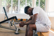 © twinsterphoto - Desperate African American male athlete sitting on bench during break in fitness training in modern gym