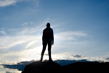 Wall Mural - young woman traveler with backpack standing on the top of the rock at summer sunset. travel and adve